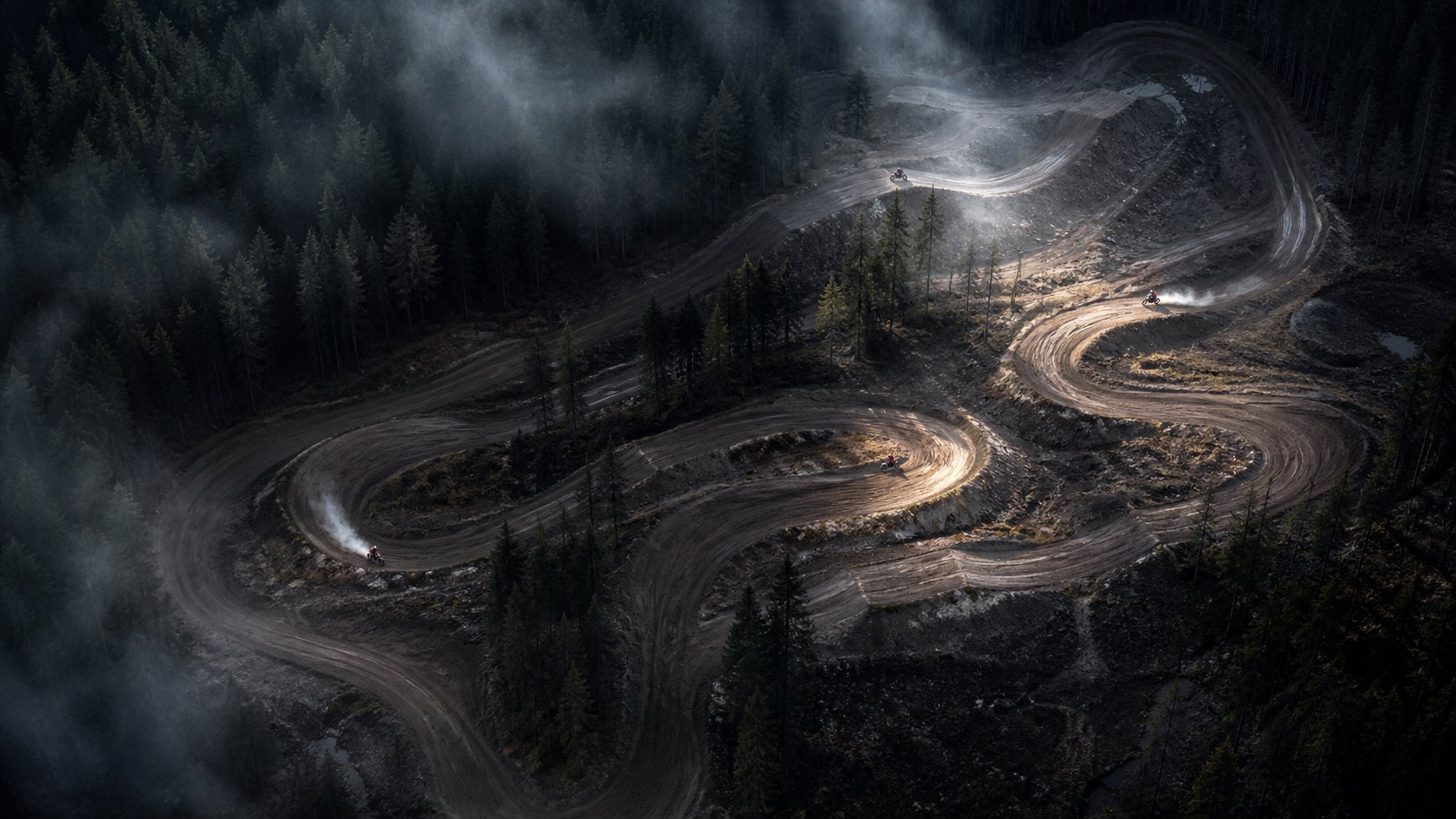 Aerial view of four motocross rides across a winding forest circuit